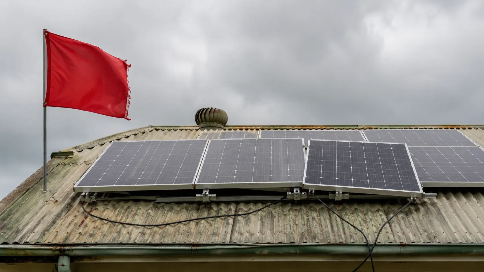 Red warning flag beside a poorly installed solar array on a weathered tin roof